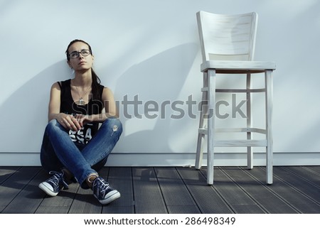 beautiful girl in casual clothes sitting on the floor, dreaming, peacefully, near a chair, outdoor, in cafe, in mall