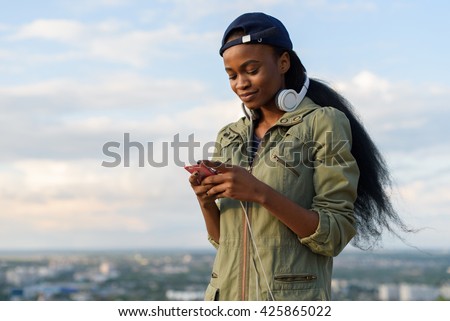 Charming african american girl listen to music and relaxing. Smiling young black lady on blurred city background