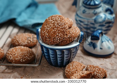 Fresh baked oatmeal cookies with sesame seeds in a cup. Sesame chip cookies on the grid for baking and blue tea set on the table. Preparation for tea drinking