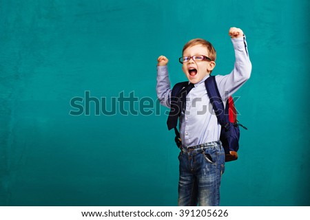 Adorable smiling little kid with big backpack jumping and having fun against blue wall. Looking at camera. School concept. Back to School