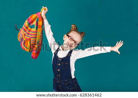 Funny little girl with big backpack jumping and having fun against turquoise wall. School concept. Back to School. School\'s out for summer. Celebrating the end of another successful school year