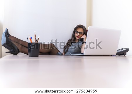 Relax business woman talking on phone and using her laptop sitting at her desk in her office with feet on the table