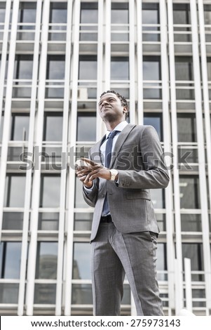 Handsome african american businessman with smart phone looking up. Behind building with windows