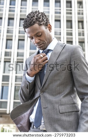 Well dressed african american business man adjusting his neck tie. Behind building with windows