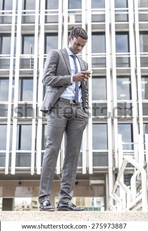 Handsome african american businessman reading email on smart phone. Behind building with windows.