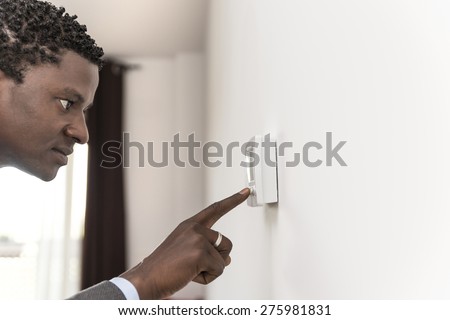 African american man push button digital thermostat  at house