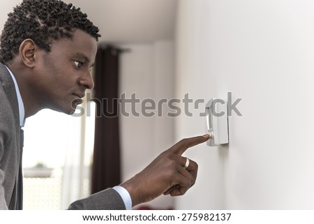 African american man push button digital thermostat at house