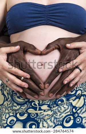 Pregnant mother Caucasian woman ethnic black African-American man father make a heart on her pregnant belly