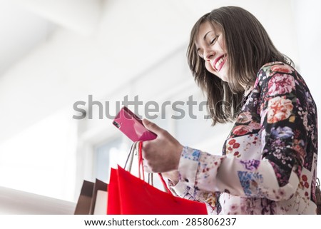 Young woman looking mobile phone, shopping and holding shopping bags