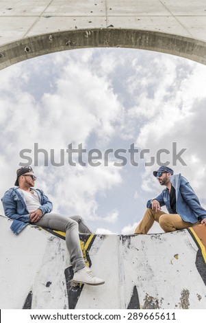 Taking the time to talk to your friend . Two handsome young men talking to each other while sitting on a wall