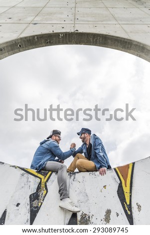 Taking the time to talk to your friend . Two handsome young men talking to each other while sitting on a wall