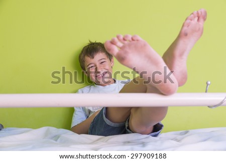 Little kid smiling with dirty feet and sitting at bed, posing on green background close-up
