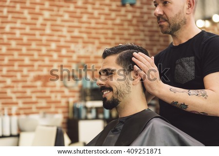 Hairstylist making men\'s haircut to an attractive man in the beauty salon.