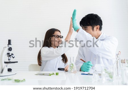 Adult Asian man and African American girl doing tests of plants in classroom. Group of diversity scientists learning science and doing analysis for germs and bacteria with microscope in the laboratory