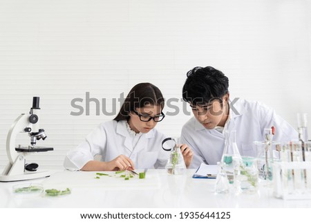 Asian man scientists and child girl doing tests of plants with magnifying in classroom. Group of scientists learning science and doing analysis for germs and bacteria with microscope and glassware