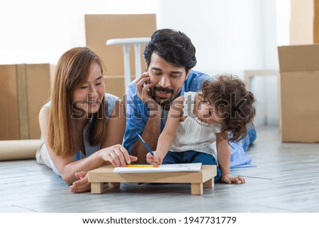 Happy father and mother lying on floor teaching little toddler girl drawing a picture or writing book with colour pencils at home. Father and mother spending time with little daughter in living room
