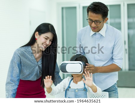 Father and mother are teaching their daughter wearing virtual reality headset at home, Future technology for children concept.