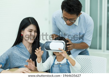 Father and mother are teaching their daughter wearing virtual reality headset at home, Future technology for children concept.
