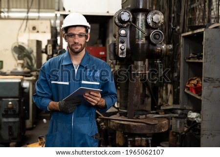Portrait of engineer male worker wear safety uniform, helmet, goggles and holding digital tablet standing near machine lathe metal at industry factory. Caucasian worker manufacturing industry concept