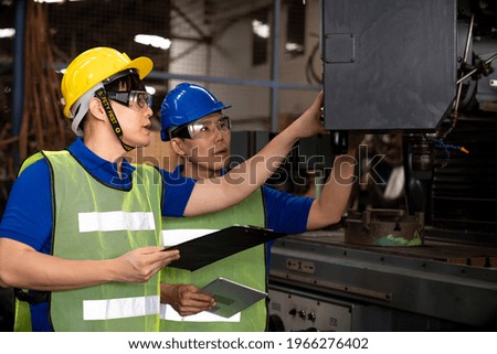 Two Asian engineer male worker maintaining machine at the industry factory. Group of Asian Factory worker check or maintenance CNC machine in industry factory