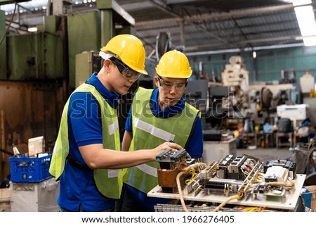 Two Asian engineer male worker maintaining electronics of machine at the industry factory. Group of Asian Factory worker check or maintenance CNC machine in industry factory