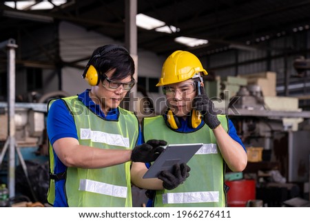 Asian factory male worker discussing and work with tablet for maintenance machine lathe metal in the industry factory. Engineer worker using manual document for lathe machine in the factory