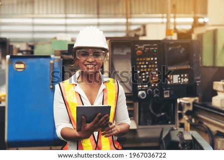 Factory woman worker at work in the industry factory, work with digital tablet with happy and smile. Female worker maintaining machine in the industrial plant