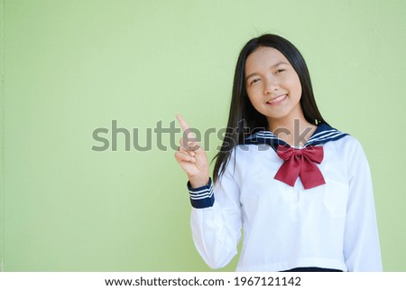 Student young girl in uniform and green background point finger up and copy space.