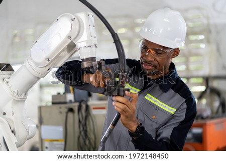 African American male engineer worker maintenance automatic robotic arm machine in factory. Black male technician worker checking, repair automatic robot hand machine with screwdriver in smart factory