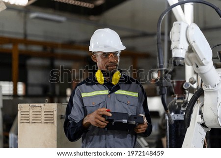 Male engineer holding robot controller for maintenance or repair automatic robotic machine in factory. Male technician worker working with control automatic robot arm system welding in the factory