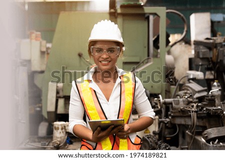 Woman factory worker at work in the industry factory, working with digital tablet with happy and smile. Female worker maintaining machine in the industrial plant