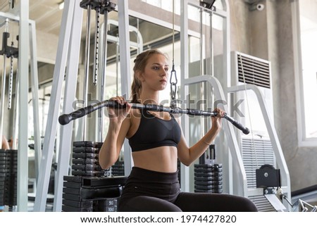 Young woman doing exercise on a lat machine in the gym. Women wear sportswear flexing arm muscles on cable machine in gym