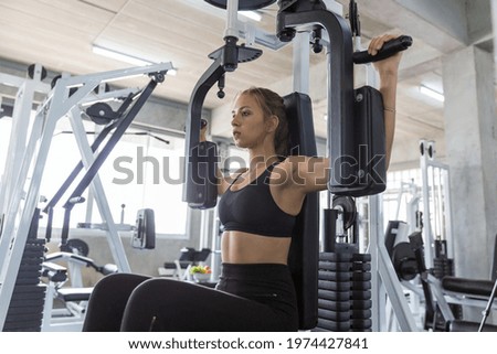 Young woman doing exercise on a chest machine fly in the gym. Women wear sportswear flexing arm muscles on chest machine fly in gym
