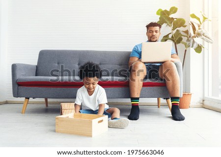 African American little boy playing with toy wooden while father working with computer laptop on sofa at home