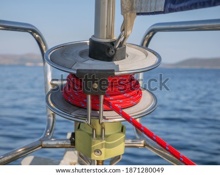 A closeup of a furling drum with red rope against a blurry sea