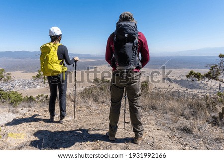 Back view of young hikers with backpacks standing on top of a hill enjoying beautiful nature scenes