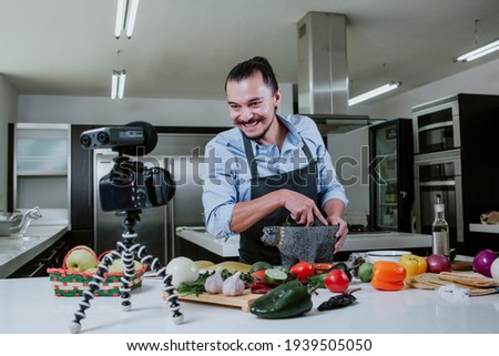 latin man food blogger preparing mexican sauce, cooking and culinary skills concept. man shooting video of himself using camera on tripod in Mexico city