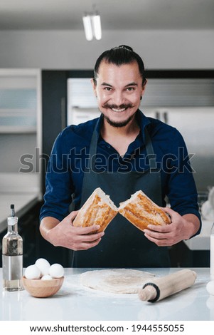 portrait of Latin man baking and holding bread at kitchen in Mexico city