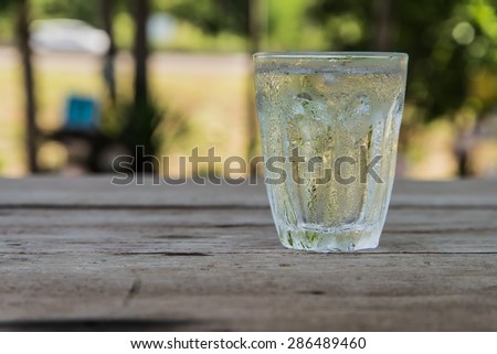 Glass of cold water, put the right on a wooden table. Focus on water drops on the glass with drops of water on the table.