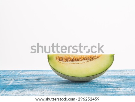 Green melon cut in half placed on a wooden floor in blue and white on the right. Fuzzy white background Focus on top melon.