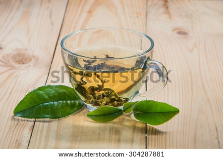 Tea and fresh tea leaves put on a light wood floor. Focus on the tea leaves and glass.