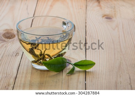 Tea and fresh tea leaves left on the ground, light wood, focus on the tea leaves and glass.