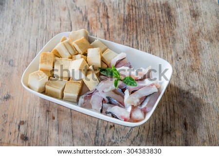 Meat, fish and tofu dish in white placed on a wooden table. Focus on fish.