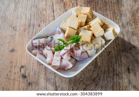 Meat, fish and tofu dish in white placed on a wooden table. Focus on fish.