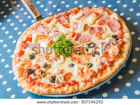 Hawaiian Pizza and Seafood In white plate placed on a blue and white striped fabric. The background is blurred and poor light.