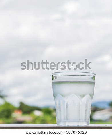 Cold water in a glass Vertical take place right on the white wood. In the background is blurred cloud and poor light.