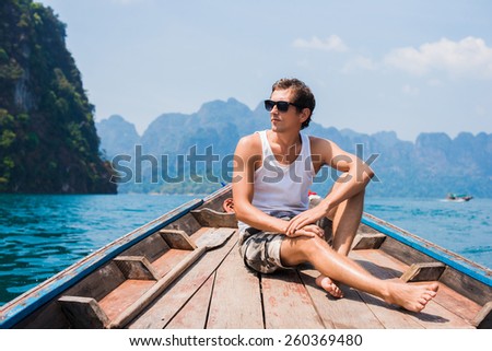 Young man in sunglasses floating in a boat on the lake with mountains in background