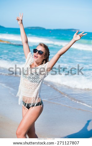 sexy girl in a black bikini and a white ?ape and sunglasses walks along the beach near the sea