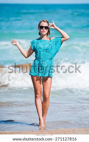 sexy girl in a black bikini and a blue ?ape and sunglasses walks along the beach near the sea