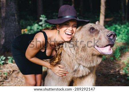 Sexy smiling girl in black evening dress posing with a wild bear